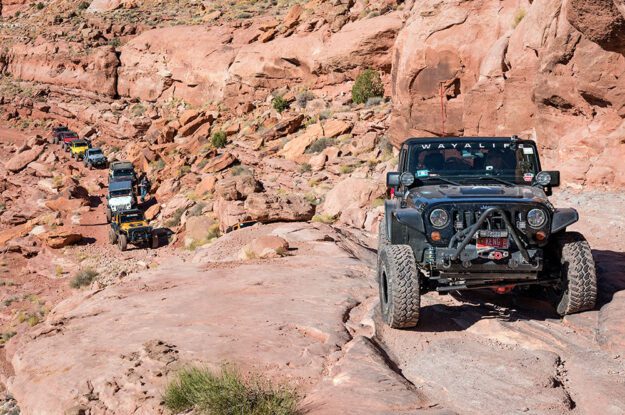 One Jeep up on rock wall and string of Jeeps below.