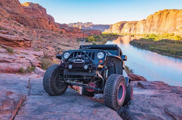 Jeep climbing rocks with a river in the background.
