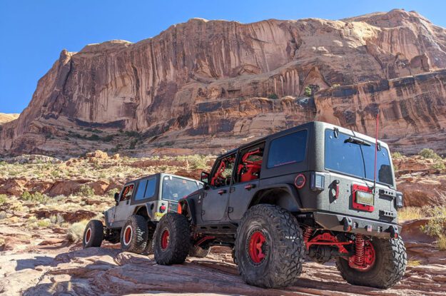 Two Jeeps with cliffs in the background.