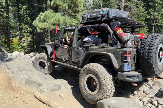 Jeep with tires wedges between large rocks.