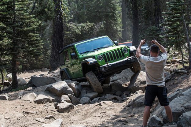 Trail guide directing green Jeep through rocky section.