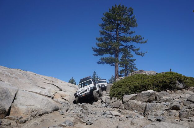 Two white jeeps coming down rocky section.