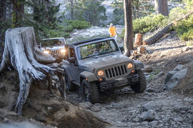 Two Jeeps drive up rocky road with Trail Guide behind.