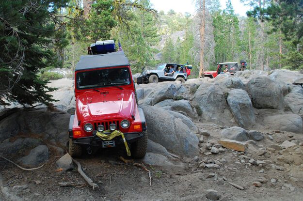 REd Jeep descends rocks while other Jeeps wait.