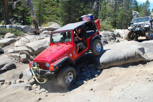 Red Jeep with an American flag descending rocks.