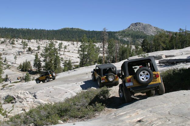 Three gold jeeps descending rock slabs.