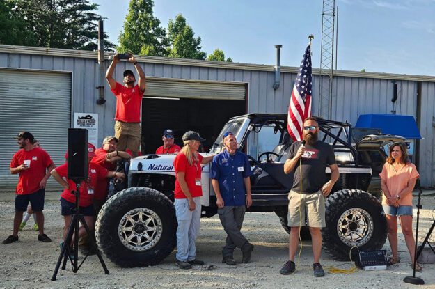 Sean talking in front of jeep and flag